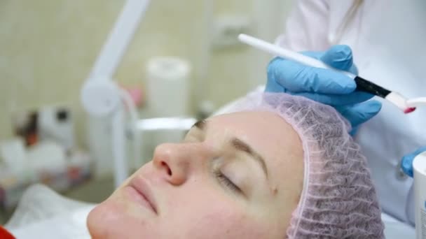 美容師は女性の顔にブラシでジェルマスクを広げます。顔の改装 — ストック動画