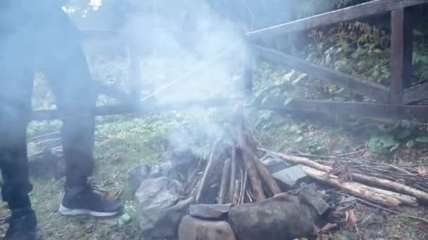 Mladý samec dělá malý lesní táborák pomocí hole a zahřívá si ruce — Stock video