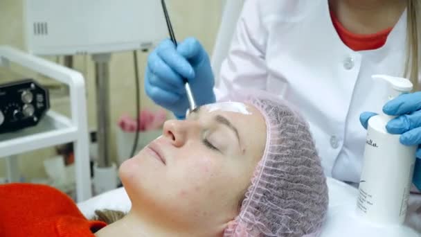 Kosmetikerin verteilt Schaumstoffmaske mit Pinsel auf weibliches Gesicht. Gesichtssanierung — Stockvideo