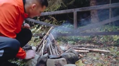 Kafkas atletik genç adam şenlik ateşine sert bir şekilde üflüyor. Duman var. 