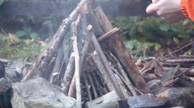 Genç erkek, çubuklarla küçük bir orman kamp ateşi yakıyor ve ellerini ısıtıyor.