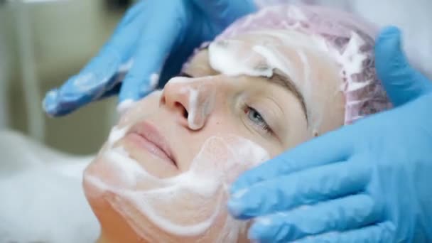 Woman getting professional facial procedure. Beautician spreads foam on face — Stock Video