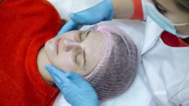 Kadın profesyonel yüz prosedürü yaptırıyor. Güzellik uzmanı yüzüne köpük sürer.