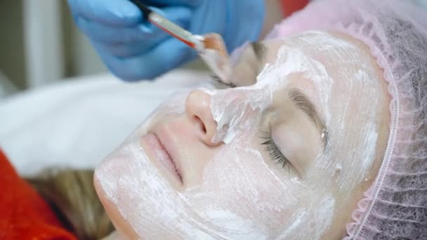 Schoonheidsspecialiste spreidt schuim masker op vrouwelijke gezicht met borstel. gezichtsrenovatie — Stockvideo