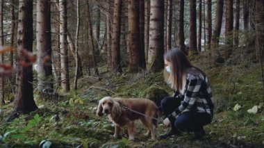 Ormanda maskeli bir kız ormanda köpeğini cocker spaniel ile okşuyor.