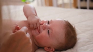 Baby girl lies on side on big white parent bed. Newborn child with grey eyes and plump cheeks lies in bedroom putting his fingers in his mouth and sucking his fingers. High quality 4k footage