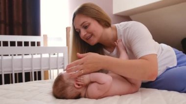 Caring mother and baby are playing in bed in the morning. Baby rolls over and crawls, mother returns him back, baby laughs. High quality 4k footage