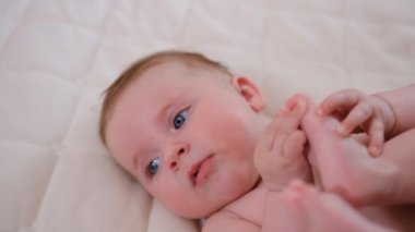 Portrait of a happy infant baby on the bed pulling his leg into his mouth, eight months old. Laughing toddler kid on sofa, face close-up. High quality 4k footage