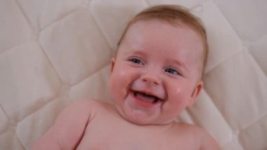 Close up of happy newborn baby smiling and gesturing while lying in bed with white linen. Adorable little baby boy with blue eyes. High quality 4k footage