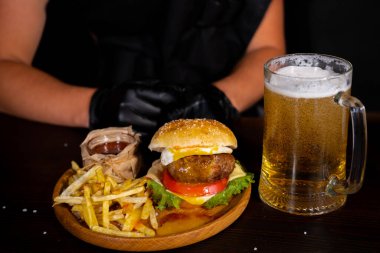 Set of hamburger beer and french fries. A standard set of drinks and food in the pub, beer and snacks. Dark background, fast food. Traditional american food. High quality photo
