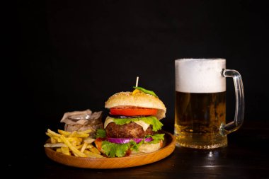 tasty hamburger burger sandwich with french fries and ketchup on a wooden tray a glass of cool beer with foam fast food black background. High quality photo
