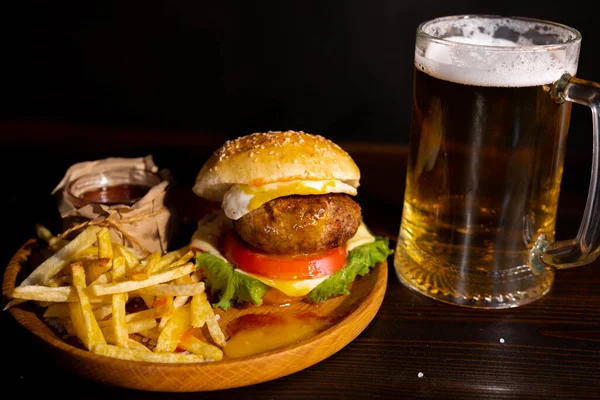 Set of hamburger beer and french fries. A standard set of drinks and food in the pub, beer and snacks. Dark background, fast food. Traditional american food. High quality photo