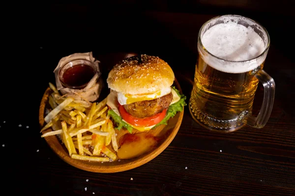 Set of hamburger beer and french fries. A standard set of drinks and food in the pub, beer and snacks. Dark background, fast food. Traditional american food. High quality photo