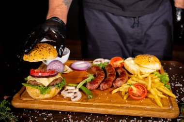 fast food burger potatoes fries sausages cutlets ketchup tomatoes onions peppers mushrooms on a wooden board on the table top view barbecue mix