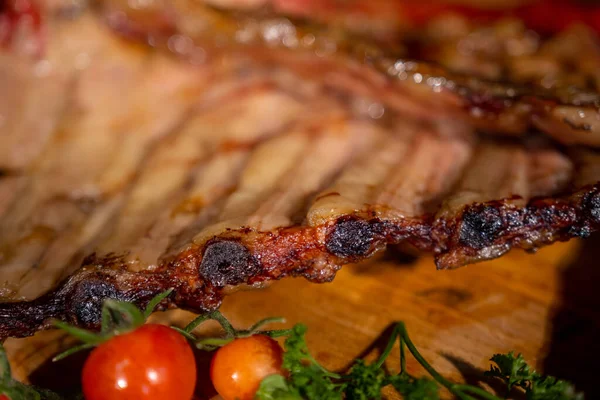 Closeup of pork ribs grilled with BBQ sauce and caramelized in honey. Tasty snack to beer on a wooden Board for filing on dark concrete background. High quality photo