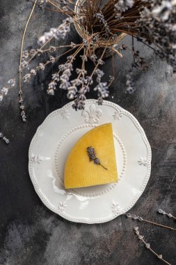 Beyaz tabakta otlu bir parça peynir. Kuru fesleğen ve lavanta çiçekli vander peyniri. dikey görüntü. Üst Manzara. metin için yer.