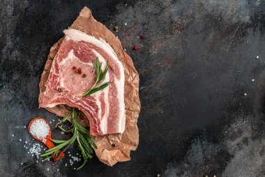 Esmer arka planda baharatlı ve otlu çiğ et. Çiğ domuz eti, pirzola. Restoran menüsü, diyet, yemek kitabı tarifi. Üst görünüm.
