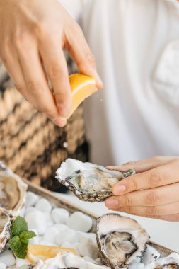 Bir adamın elleri çiğ bir istiridyenin üzerine taze limon suyu sıkıyor. Yaşam tarzı, yemeye hazır. Restoranda şampanyayla istiridye yemeği.