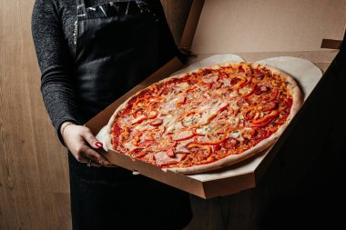 Kutuda pizza tutan kadın eller. Teslimat kutusunda sıcak büyük pepperonili pizza. İtalyan pizzası.
