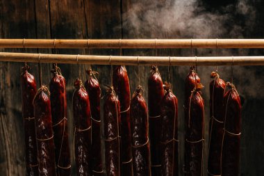 Tütsühanede asılı sosis içme süreci. Duman bulutları yükselir ve sallanan sosisleri sarar. Uzun pankart biçimi,