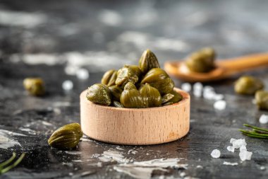 Koyu arkaplandaki kapari kavanozunda marine edildi. Akdeniz, İtalyan, İspanyol ve Fransız mutfağı için lezzetli malzemeler. Turşu, konserve kapari..