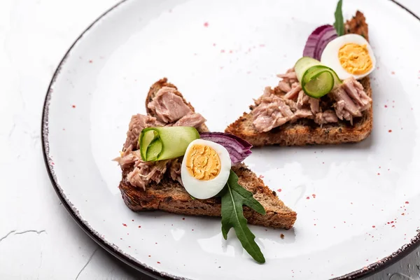 Toasts with tuna delicious healthy food, sandwiches with canned tuna and cucumber, quail eggs and onion on a white plate on a light background — Zdjęcie stockowe
