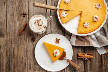 portion of delicious bright orange pumpkin open pie on plate cut from whole cake, decorated with whipped cream, with latte. banner, menu, recipe place for text, top view.