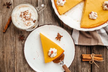 Traditional autumn dish Spicy pumpkin pie with whipped cream latte with cinnamon on black stone table. Healthy food trend. top view.