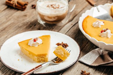 Pumpkin cheesecake, pumpkin pie with whipped cream on the wooden table. Homemade pastry for Thanksgiving.