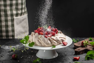 Lezzetli ev yapımı Pavlova pastası taze çilek ve krem şantili. Şefin elleri toz bulutu gibi dondurucu bir hareketle havada uçuyor. Mutfak, yemek pişirme, fırın konsepti,