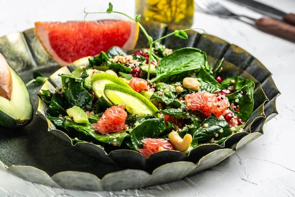 Vegan winter salad by chef hand in home kitchen with quinoa, spinach, avocado, grapefruit, pomegranate, nuts and microgreens.