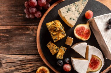 Lezzetli gurme peyniri, dilimlenmiş taze incir ve üzümlerle servis edilen yumuşak peynirlerin kırsal ahşap arka planda servis edilmesi, yemek servisi, afiş, menü, tarif, metin için yer.
