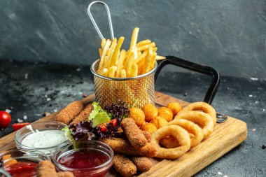 Mozarella çubukları, soğan halkaları, patates kızartmaları, tavuk külçeleri ve ahşap bir tahtanın üzerindeki sosu çıkarın. afiş, menü, metin için tarif yeri.