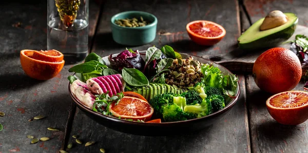 Healthy vegetarian buddha bowl salad with vegetables and fruit avocado, blood orange, broccoli, watermelon radish, spinach, quinoa, pumpkin seeds, Vegan, detox green Buddha bowl recipe.