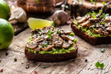 Avokado tostu, mantar ve mikroyeşil tam tahıllı sandviç. Susam ile süslenmiş. Vejetaryen yemeği. Vejetaryen menüsü. Lezzetli kahvaltı ya da atıştırmalık, temiz yemek, diyet, vejetaryen yemek konsepti. en üstteki görünüm.