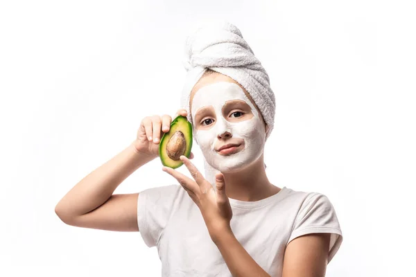 水疗少女 戴着面容美丽的面具 手里拿着半个新鲜鳄梨 与白色隔离 温泉治疗的概念 面部护理 复制空间 — 图库照片
