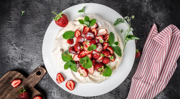 delicious homemade Pavlova cake with fresh strawberries and whipped cream. Female baker decorating delicious meringue cake, top view. place for text,