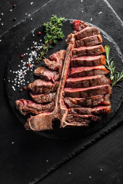Bir parça pişmiş T-bone ya da yıllanmış wagyu bifteği ızgara biftek ve taş tahtada servis edilmiş baharatlar. dikey görüntü. metin için yer,