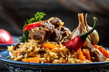 Pilav denilen geleneksel Özbek yemeği. Tabakta et ve siyah ahşap arka planda doğu süsü olan pirinç, uzun afiş formatı. Metin için boşluk.