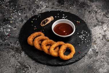 Ev yapımı kızarmış soğan halkaları, taş tahtada domates sosu, Amerikan sağlıksız kalori yemeği. Lezzetli bir bar tarzı, aperatif, restoran menüsü, üst manzara.,