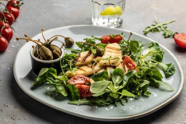 Izgara halloumi peynirli taze salata, domates, kapari, marul ve roka. Ketojenik paleo diyeti. Lezzetli kahvaltı veya atıştırmalık, temiz yemek, diyet, vejetaryen yemek konsepti.