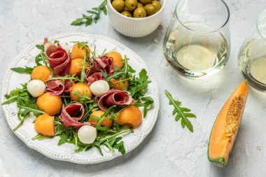 Akdeniz salatası jambon, mozzarella ve yeşil fesleğen yaprakları ve kavun kavunu beyaz masada, geleneksel İspanyol ve İtalyan aperatifi toptan Grissini ile servis edilir.,