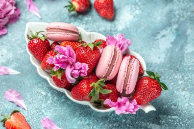 Pembe şakayık çiçeği ve makarna kurabiyeleri ve mavi arka planda tatlı çilek. Meyveli küçük Fransız pastaları. en üstteki görünüm.