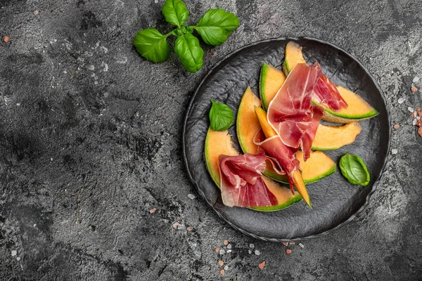 Summer appetizer with sweet melon and prosciutto and basil. Antipasti, Traditional Spanish and Italian appetizer. Top view on white stone table, Long banner format. top view,