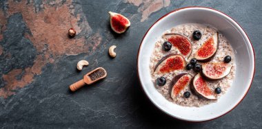 Lezzetli yulaf ezmesi, incir parçalarıyla süslenmiş, bir kasede çilek ve chia tohumları, sağlıklı kahvaltı glüten, laktozsuz, fitness yiyeceği. Uzun pankart biçimi, üst görünüm.