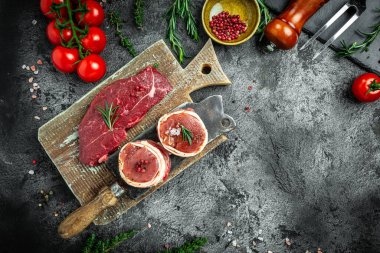 Çiğ mermer et, biftek fileminyonu. Koyu beton arka planda pastırmaya sarılı kırmızı biftekler. Et ürünleri paketlendi.