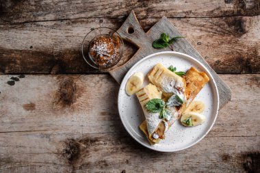 Çikolata kaplı krepler ve beyaz tabakta muz. İnce krep, blini. Lezzetli kahvaltı ya da atıştırmalık. Yemek tarifi geçmişi. Kapat..
