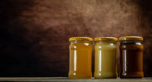 ダーククリームの異なる種類の瓶のコレクション 蜂蜜の3つの瓶と組成物 ロングバナー形式 — ストック写真