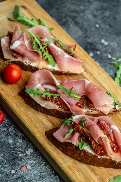 Kurutulmuş domatesler, prosciutto ve roka ile ahşap bir tahtanın üzerinde. Lezzetli kahvaltı..