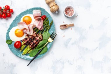 Kahvaltıda yumurta, pastırmaya sarılmış kuşkonmaz, jambon, domates ve salata. Sağlıklı dengeli yiyecekler. Üst görünüm, yukarıda, afiş.